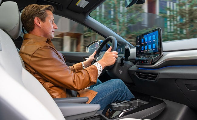 An interior view of a man driving an ID.4, with on hand on the steering wheel, and his focus on the center console display.