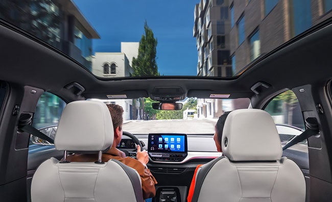 A forward shot of a man and woman driving an ID.4 with the sunshade open as they head down an urban street.