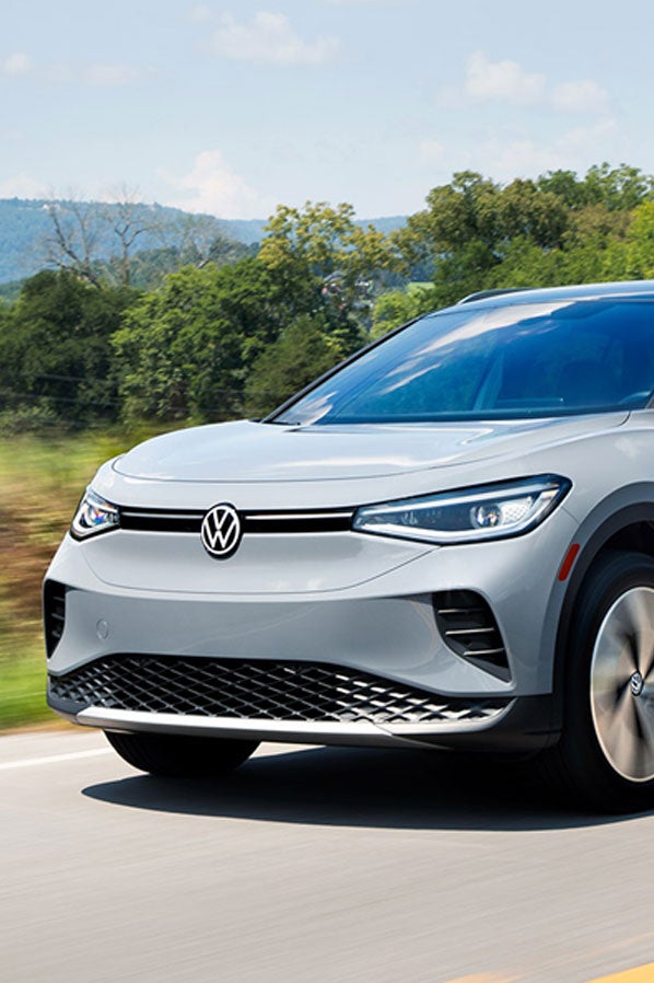 An ID.4 in Moonstone Gray drives along a highway with trees and mountains in the background.