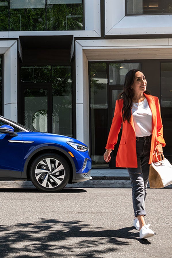 A woman walks away from an ID.4 in Dusk Blue Metallic that’s parked on an urban street.
