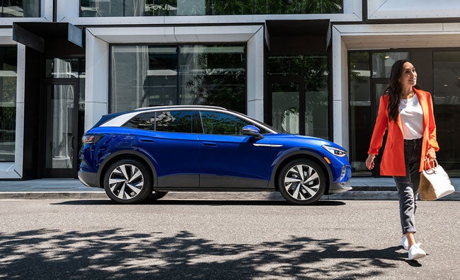 A woman walks away from an ID.4 in Dusk Blue Metallic that’s parked on an urban street.