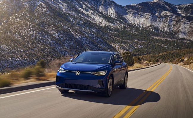 An ID.4 in Dusk Blue Metallic drives along a two-lane highway with mountains in the background.