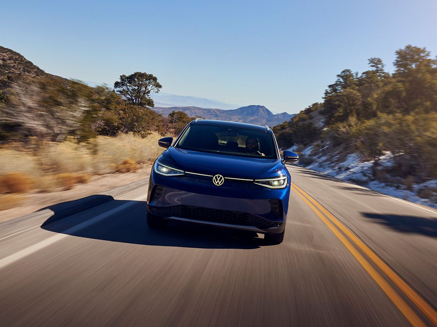 A front shot of an ID.4 in Dusk Blue Metallic cruising down a 2-lane highway in a natural setting.